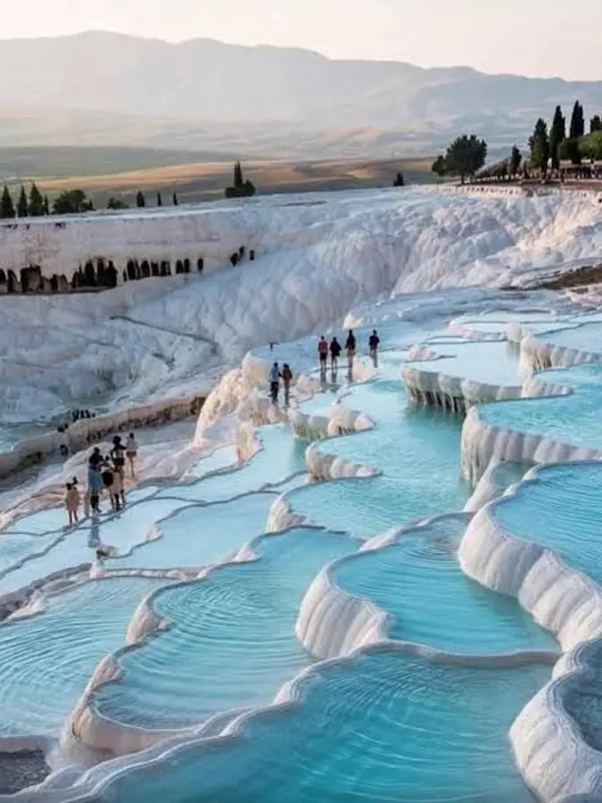 Visitors walking barefoot down the white travertine terraces at Pamukkale, with shallow water in the basins